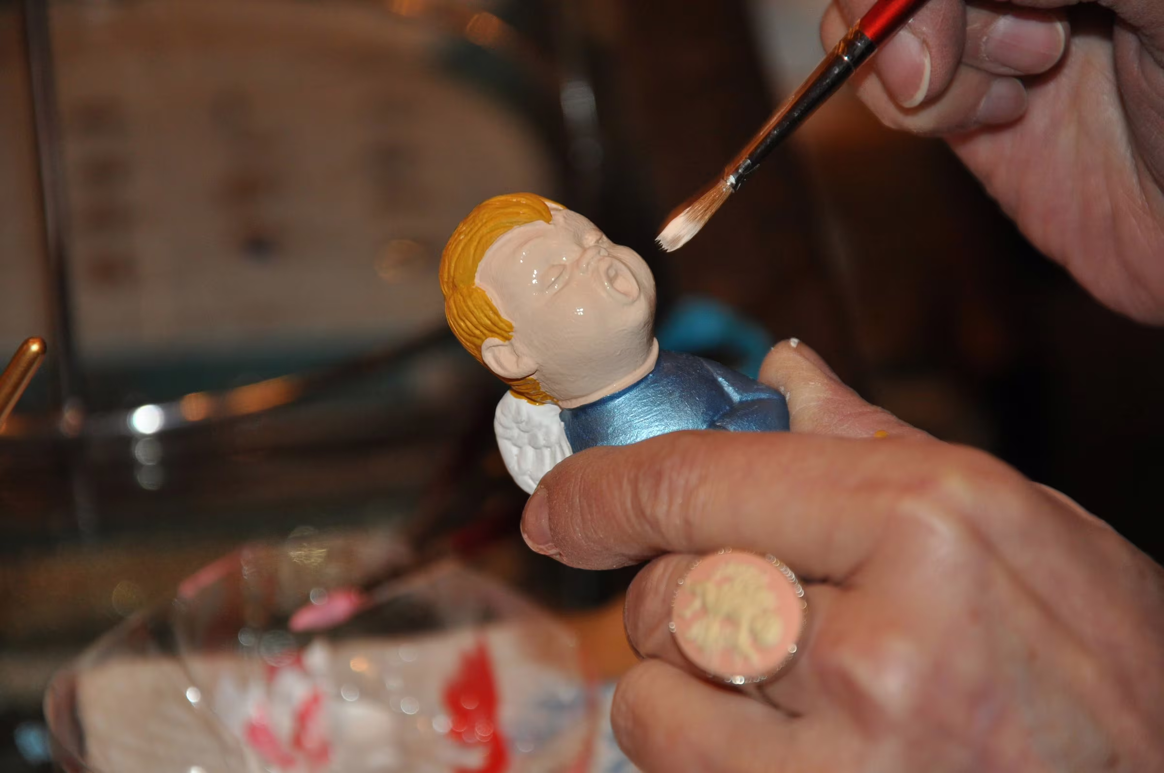 Des mains peignent un ange choriste au pinceau, à l'Atelier.